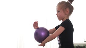 Una niña de gimnasia rítmica en un traje negro realiza ejercicios con una  pelota