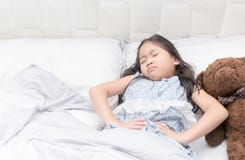 Una niña en su cama tiene un dolor de estómago foto de archivo Una niña en su cama tiene un dolor de estómago foto de archivo
