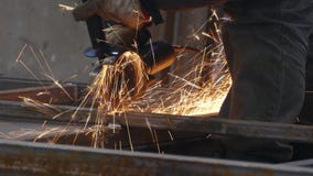 Una persona trabaja con una amoladora Corta las estructuras de acero en la fábrica Las chispas hermosas vuelan hacia fuera almacen de metraje de vídeo Una persona trabaja con una amoladora Corta las estructuras de acero en la fábrica Las chispas hermosas vuelan hacia fuera almacen de metraje de vídeo