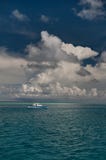 Una piccola barca bianca in mezzo all'acqua dell'oceano del turchese più pura sotto il cielo con i bei cumuli bianchi, f vertical Fotografia Stock Una piccola barca bianca in mezzo all'acqua dell'oceano del turchese più pura sotto il cielo con i bei cumuli bianchi, f vertical Fotografia Stock