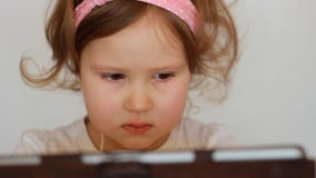 Una piccola ragazza sveglia in cuffie esamina il PC della compressa del monitor dello schermo Bambino divertente che guarda TV, v archivi video Una piccola ragazza sveglia in cuffie esamina il PC della compressa del monitor dello schermo Bambino divertente che guarda TV, v archivi video
