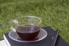 Una pluma, un cuaderno, y una taza de té en el césped fotos de archivo Una pluma, un cuaderno, y una taza de té en el césped fotos de archivo