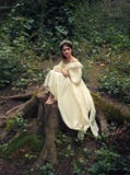 Una princesa joven, triste con el pelo muy largo se sienta en un tocón grande de un árbol viejo y espera a su príncipe La muchach foto de archivo Una princesa joven, triste con el pelo muy largo se sienta en un tocón grande de un árbol viejo y espera a su príncipe La muchach foto de archivo