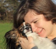 Una ragazza con peli marroni lunghi tiene un piccolo cane simile a pelliccia - il suo animale domestico fotografia stock Una ragazza con peli marroni lunghi tiene un piccolo cane simile a pelliccia - il suo animale domestico fotografia stock