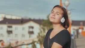 Una ragazza in cuffie bianche con piacere ascolta musica su una sera calda dell'estate stock footage Una ragazza in cuffie bianche con piacere ascolta musica su una sera calda dell'estate stock footage