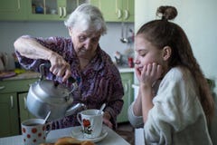 Una señora mayor trata un desayuno de la niña, sentándose en la tabla en su casa foto de archivo libre de regalías Una señora mayor trata un desayuno de la niña, sentándose en la tabla en su casa foto de archivo libre de regalías
