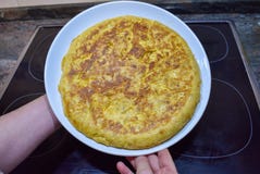 una tortilla española sabrosa con las patatas, cebolla y huevos, apenas cocinados en un sartén negro en una cocina y mostrar de i fotografía de archivo una tortilla española sabrosa con las patatas, cebolla y huevos, apenas cocinados en un sartén negro en una cocina y mostrar de i fotografía de archivo