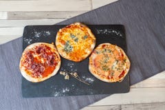 Una vista aerea di tre pizze su un contorno nero del bordo con farina ed il fiore asciutto immagine stock Una vista aerea di tre pizze su un contorno nero del bordo con farina ed il fiore asciutto immagine stock