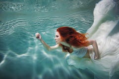 Underwater girl. Beautiful red-haired woman in a white dress, swimming under water. stock photos Underwater girl. Beautiful red-haired woman in a white dress, swimming under water. stock photos