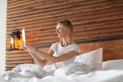 Une femme de sourire se trouve sur le défilement de lit par son comprimé images stock Une femme de sourire se trouve sur le défilement de lit par son comprimé images stock