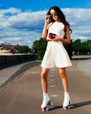 Une fille asiatique incroyable dans des lunettes de soleil et un équipement lumineux d'été posant sur des patins de rouleau avec images stock Une fille asiatique incroyable dans des lunettes de soleil et un équipement lumineux d'été posant sur des patins de rouleau avec images stock