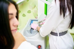 Une fille se situe dans le bureau de l'esthéticien, les mains du docteur tiennent un dispositif pour l'épilation de laser image stock Une fille se situe dans le bureau de l'esthéticien, les mains du docteur tiennent un dispositif pour l'épilation de laser image stock