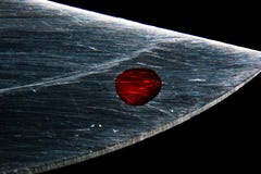 Une goutte de sang sur la lame d'un macro de couteau image stock Une goutte de sang sur la lame d'un macro de couteau image stock