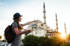 Une jeune belle fille de voyageur dans un chapeau avec un sac à dos et une carte à côté de la mosquée bleue est une vue célèbre à Images stock Une jeune belle fille de voyageur dans un chapeau avec un sac à dos et une carte à côté de la mosquée bleue est une vue célèbre à Images stock