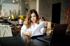 Une jeune, bien disposée femme, pas une musculation à tête mince, s'assied dans un café confortable, travaille à un ordinateur, e photo libre de droits Une jeune, bien disposée femme, pas une musculation à tête mince, s'assied dans un café confortable, travaille à un ordinateur, e photo libre de droits