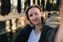 Une jeune femme de sourire se tient en parc et fait un selfie La fille prend des photos d'elle-même Portrait femelle photographie stock Une jeune femme de sourire se tient en parc et fait un selfie La fille prend des photos d'elle-même Portrait femelle photographie stock