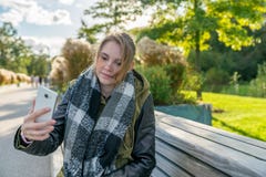 Une jeune femme prend un selfie sur un banc en parc image stock Une jeune femme prend un selfie sur un banc en parc image stock