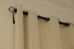 Une partie des rideaux gris de la mati?re sur un tuyau noir dans la chambre sur le mur photographie stock Une partie des rideaux gris de la mati?re sur un tuyau noir dans la chambre sur le mur photographie stock