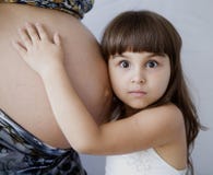 Une petite fille blanche étreint le ventre de sa mère enceinte Les yeux de l'enfant sont grands ouverts dans la surprise images stock Une petite fille blanche étreint le ventre de sa mère enceinte Les yeux de l'enfant sont grands ouverts dans la surprise images stock