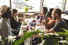 Une soci?t? des jeunes multiculturels dans un caf? mangeant de la pizza, cocktails potables, ayant l'amusement images stock Une soci?t? des jeunes multiculturels dans un caf? mangeant de la pizza, cocktails potables, ayant l'amusement images stock