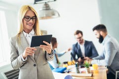Ung affärskvinna som använder den digitala minnestavlan medan kollega i bakgrund royaltyfri bild Ung affärskvinna som använder den digitala minnestavlan medan kollega i bakgrund royaltyfri bild