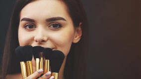 Ung attraktiv kvinna för makeupkonstnär som rymmer borstar och arrangerar i en studio på en svart bakgrund Under denna tid honom lager videofilmer Ung attraktiv kvinna för makeupkonstnär som rymmer borstar och arrangerar i en studio på en svart bakgrund Under denna tid honom lager videofilmer