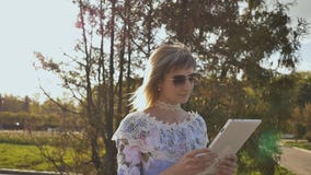 Ung flicka som använder den utomhus- minnestavlan och att le Flicka som använder digital minnestavlaPC i parkera Student som anvä lager videofilmer Ung flicka som använder den utomhus- minnestavlan och att le Flicka som använder digital minnestavlaPC i parkera Student som anvä lager videofilmer