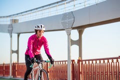 Ung kvinna i cykel för väg för rosa färgomslagsridning på brocykellinjen i den kalla Sunny Autumn Day Sund livsstil royaltyfri foto Ung kvinna i cykel för väg för rosa färgomslagsridning på brocykellinjen i den kalla Sunny Autumn Day Sund livsstil royaltyfri foto