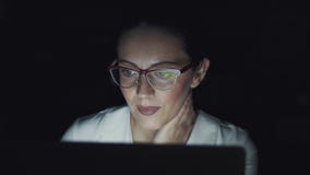 Ung kvinna som sent arbetar på en bärbar dator i aftonen Stående av en affärskvinna med exponeringsglas i ett mörkt rum stock video Ung kvinna som sent arbetar på en bärbar dator i aftonen Stående av en affärskvinna med exponeringsglas i ett mörkt rum stock video