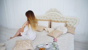 Ung kvinna som är lycklig med tillståndet av hår som sitter med tillbaka till kameran på mjuk säng royaltyfria foton Ung kvinna som är lycklig med tillståndet av hår som sitter med tillbaka till kameran på mjuk säng royaltyfria foton