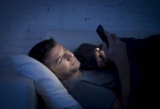 Ung man i sängsoffa hemma sent på natten som smsar på mobiltelefonen i kopplat av lågt ljus royaltyfri bild Ung man i sängsoffa hemma sent på natten som smsar på mobiltelefonen i kopplat av lågt ljus royaltyfri bild
