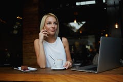 Ung ursnygg kvinna som har smart telefonkonversation, medan sitta framme av den öppna bärbar datordatoren i kaféstång arkivbilder Ung ursnygg kvinna som har smart telefonkonversation, medan sitta framme av den öppna bärbar datordatoren i kaféstång arkivbilder