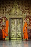 unga buddistiska munkar som framme viker en orange textil av en utmärkt dekorerad guld- pläterad trädörr royaltyfri foto unga buddistiska munkar som framme viker en orange textil av en utmärkt dekorerad guld- pläterad trädörr royaltyfri foto