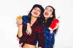 Unga hipsterflickor som har gyckel som dricker en sodavatten från sugrör och innehav en hamburgare, ett lyckligt leende och ett s arkivbild Unga hipsterflickor som har gyckel som dricker en sodavatten från sugrör och innehav en hamburgare, ett lyckligt leende och ett s arkivbild