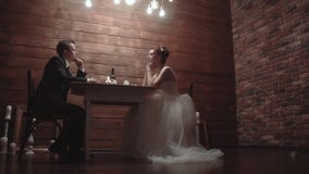 Unga par i en gifta sig dress som sitter i en restaurang och talar, under matst?lle l?ngsam r?relse arkivfilmer Unga par i en gifta sig dress som sitter i en restaurang och talar, under matst?lle l?ngsam r?relse arkivfilmer