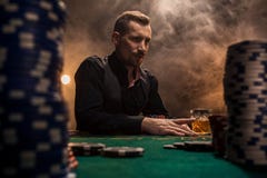 Ungt stiligt mansammanträde bak pokertabellen med kort och chiper royaltyfri bild Ungt stiligt mansammanträde bak pokertabellen med kort och chiper royaltyfri bild