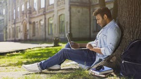 University student under tree, using laptop looking surprised, upsetting news Royalty Free Stock Photography University student under tree, using laptop looking surprised, upsetting news Royalty Free Stock Photography