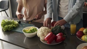 Unrecognizable young couple`s hands cooking together a healty meal. Plenty of various colorful vegetables on the kitchen