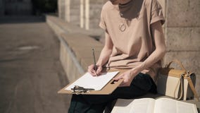 Unrecognizable young woman writing with a pencil outside on summer day