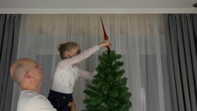 Uomo adulto e ragazza caucasici che decorano l'albero di Natale - disporre cappello a cilindro rosso sopra l'albero di abete deco stock footage Uomo adulto e ragazza caucasici che decorano l'albero di Natale - disporre cappello a cilindro rosso sopra l'albero di abete deco stock footage