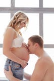 Uomo bello che bacia la pancia della sua bella moglie incinta fotografia stock Uomo bello che bacia la pancia della sua bella moglie incinta fotografia stock