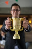Uomo d'affari asiatico che tiene una tazza dorata del trofeo ad allegro e celebrata il suo riuscito nella carriera e nella missio fotografie stock libere da diritti Uomo d'affari asiatico che tiene una tazza dorata del trofeo ad allegro e celebrata il suo riuscito nella carriera e nella missio fotografie stock libere da diritti