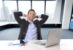 Uomo d'affari attraente felice al lavoro d'ufficio che si siedono allo scrittorio del computer soddisfatto ed a sorridere rilassa fotografia stock libera da diritti Uomo d'affari attraente felice al lavoro d'ufficio che si siedono allo scrittorio del computer soddisfatto ed a sorridere rilassa fotografia stock libera da diritti
