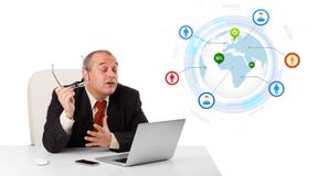 Uomo d'affari che si siede allo scrittorio e che guarda computer portatile con il globo e così Immagine Stock Libera da Diritti