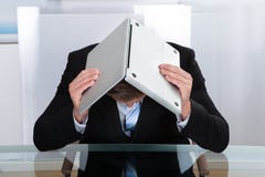 Uomo d'affari depresso che si nasconde sotto il suo computer portatile immagine stock Uomo d'affari depresso che si nasconde sotto il suo computer portatile immagine stock