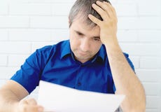 Uomo d'affari di pensiero che tocca la sua testa che tiene un documento che si siede alla tavola un uomo in vestiti di affari che fotografia stock Uomo d'affari di pensiero che tocca la sua testa che tiene un documento che si siede alla tavola un uomo in vestiti di affari che fotografia stock