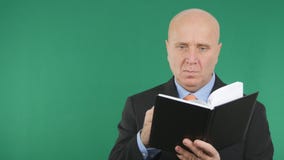 Uomo d'affari sicuro Read e scrivere nell'ordine del giorno con il fondo di schermo verde fotografia stock libera da diritti Uomo d'affari sicuro Read e scrivere nell'ordine del giorno con il fondo di schermo verde fotografia stock libera da diritti