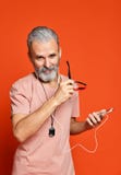 Uomo senior che ascolta la musica sulle cuffie isolate su fondo arancio immagini stock libere da diritti Uomo senior che ascolta la musica sulle cuffie isolate su fondo arancio immagini stock libere da diritti