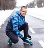 Uomo sorridente che lega i laccetti sull'eseguire le scarpe da tennis prima del funzionamento immagine stock Uomo sorridente che lega i laccetti sull'eseguire le scarpe da tennis prima del funzionamento immagine stock