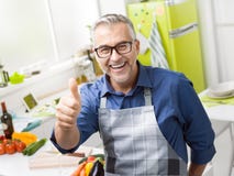 Uomo sorridente sicuro che posa nella sua cucina fotografie stock libere da diritti Uomo sorridente sicuro che posa nella sua cucina fotografie stock libere da diritti